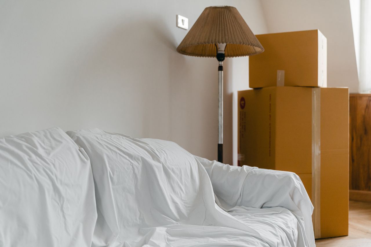 Canapé recouvert d'un drap, lampadaire et cartons emballés dans une pièce claire et spacieuse d'une maison contemporaine neuve